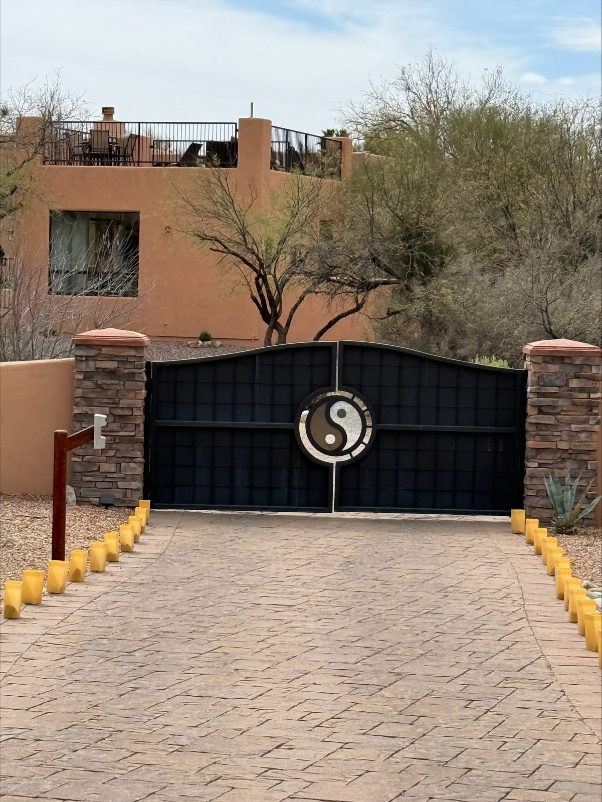 Black residential estate gate with custom stone medallion and stamped-concrete drive — Signal Gates